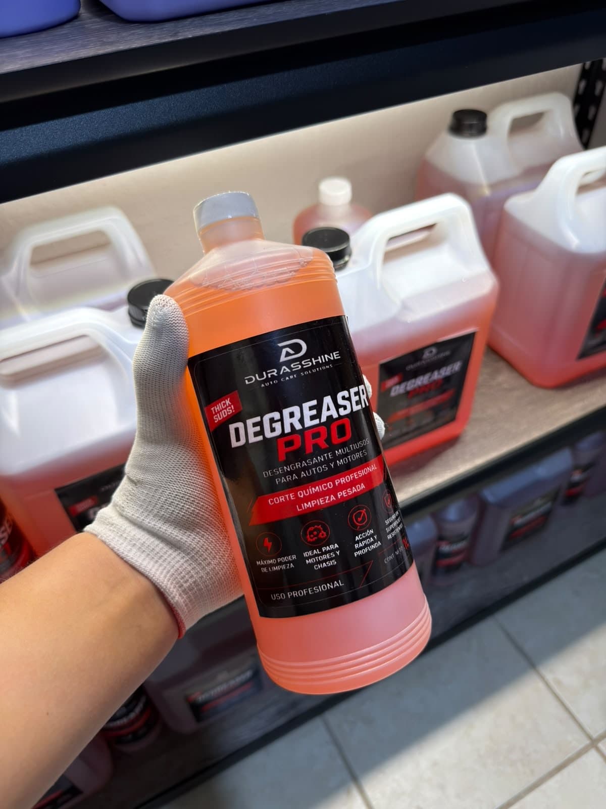 Botella de Degreaser Pro de 1 litro en la mano, frente a garrafas en la bodega