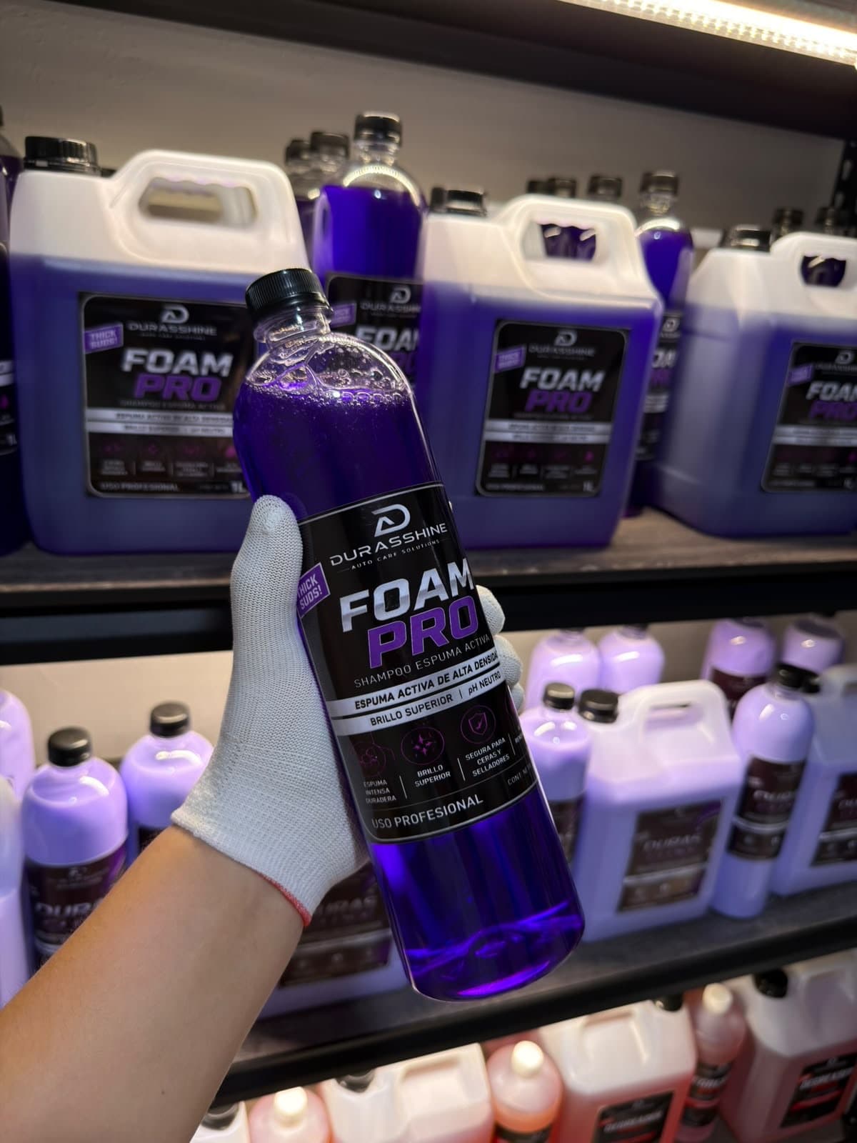 Botella de Foam Pro de 1 litro en la mano, frente a garrafas en la bodega