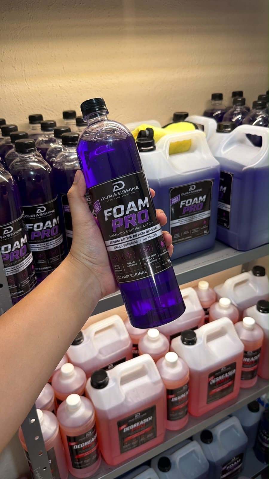 Botella de Foam Pro en la mano frente a estantes de garrafas