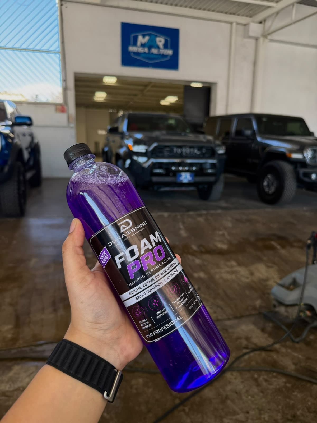 Botella de Foam Pro en la mano en un taller de lavado con camionetas